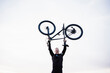 © Eva Blanco/Westend61 - Cheerful sportsman lifting bicycle against sky