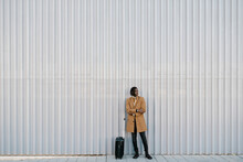 Man With Suitcase Standing Against Gray Wall While Looking Away