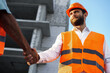 © fotofabrika - Two men engineers in workwear shaking hands against construction site.
