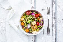 Bowl Of Zoodles With Fried Tofu, Red Quinoa, Red Onions And Tomatoes