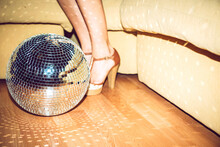 Young Woman Wearing High Heels Standing By Disco Ball On Floor In Party