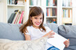 © Larissa Veronesi/Westend61 - Portrait of happy little girl sitting on the couch at home with digital tablet
