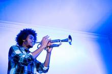 Young Male Musician Practicing Trumpet Against Wall In Blue Room