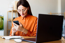 Female Freelancer Working At Home Sitting At Desk Using Smartphone