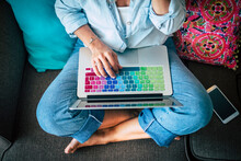 Woman Using Laptop With Multicoloured Keyboard On Couch At Home