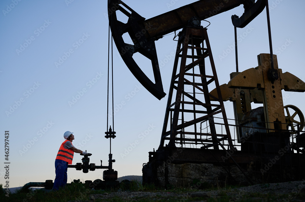 Oil Machine Operator Petroleum operator in work vest using pumping unit to extract crude oil ...