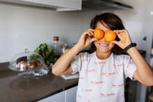 Portrait Of Smiling Boy In Kitchen Covering Eyes With Tangerines