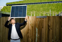 Businessman Standing At A Boarding Holding Up Solar Panel