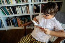 Boy With Glasses Sitting On Armchair Reading Book