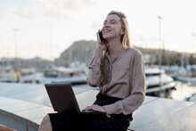 Happy Young Businesswoman Using Cell Phone And Laptop At The Waterfront