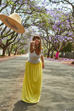 Woman Throwing A Hat In The Middle Of A Street Full Of Jacaranda Trees In Bloom, Pretoria, South Africa