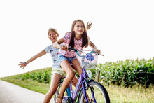 Happy Girls Riding Bicycle On A Country Lane