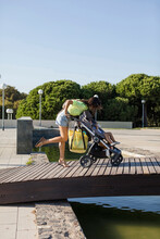 Mother With Daughter In Pram Crossing Wooden Bridge In A Park