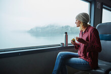 Chile, Hornopiren, Woman Looking Out Of Window Of A Ferry Eating An Avocado