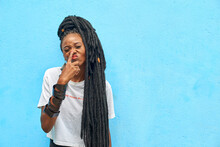 Portrait Of Woman With Long Dreadlocks Touching Her Nose In Front Of Turquoise Wall
