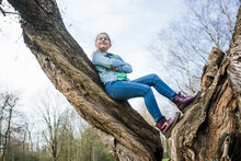 Smiling Girl With Arms Crossed Leaning On Tree Trunk In Park