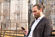 © Michelle Fraikin/Westend61 - Bearded young businessman wearing glasses looking at cell phone, New York City, USA