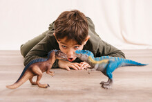 Portrait Of Little Boy Crouching On The Floor Playing With Toy Dinosaurs