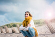 © Robijn Page/Westend61 - Mature woman crouching in the dunes, enjoying the wind