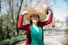 Portrait Of Mature Woman With Stack Of Straw Hats On Her Head Outdoors