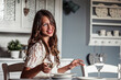 © Wilfried Feder/Westend61 - Portrait of smiling young woman sitting at laid table in country style kitchen