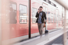 Happy Young Man With Cell Phone Walking On Station Platform Along Commuter Train