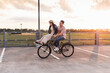 © UWE_UMSTAETTER/Westend61 - Happy young couple together on a bicycle on parking deck at sunset