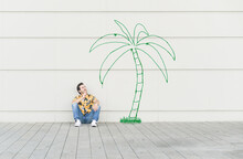 Digital Composite Of Young Man Sitting At A Palm At A Wall