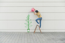 Digital Composite Of Young Man Watering Flower At A Wall