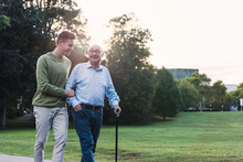 Young Man Assisting His Grandfather Walking In A Park