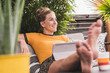 © UWE_UMSTAETTER/Westend61 - Relaxed woman sitting on couch on terrace at home using tablet