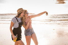 Two Girlfriends Having Fun, Walking On The Beach, Taking Smartphone Selfies