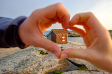 Sweden, Vastra Gotaland County, Grebbestad, Hands Of Girl Making Heart Shape Against Hut On Rocky Shore Of Tjurpannans Nature Preserve