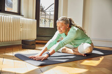 Woman Exercising While Sitting On Exercise Mat Over Floor In Living Room