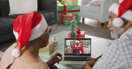 Poster - Happy african american couple on video call on laptop with santa claus in face mask at christmas