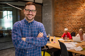 Wall Mural - Cropped shot of a businessman standing in the office with his arms folded looking confident and smiling at the camera. Portrait of successful businessman. Looking at camera with arms crossed.