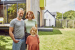 © Maya Claussen/Westend61 - Smiling family standing outside tiny house in yard