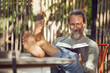 © Maya Claussen/Westend61 - Smiling bearded man reading book while relaxing on chair in yard