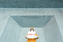 Portrait Of Man Wearing Protective Clothing Holding 'Covid 19' Sign