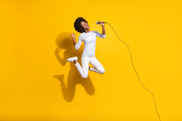 Poster - Full length photo of dark skin lady jump up sing mic wear white pants pullover isolated on yellow color background