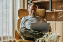 Smiling Mature Man Working On Laptop While Sitting On Chair