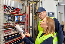 Two Electricians With Plan Looking At Fuse Box