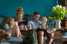 Family With Digital Tablet And Photo Album Sitting On Sofa In Living Room