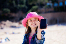 Portrait Of Grinning Little Girl Showing Her Mobile Phone On The Beach