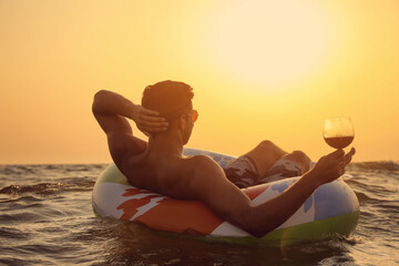 Sticker - Man with glass of wine and inflatable ring in sea at sunset