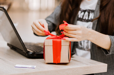 Wall Mural - The woman opens the gift. There is a laptop and a credit card on the table. Online shopping and gift concept