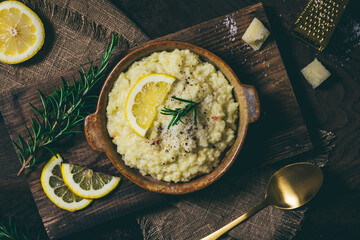 Wall Mural - Lemon rice risotto with rosemary and fresh lemon slices on dark wooden background, top view