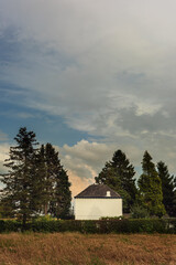 Wall Mural - White country house among trees in a field under a blue cloudy sky.