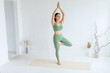 © Вадим Каштанов - Happy young woman in green sportswear practices yoga in Tree pose. Home yoga.