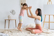 © Вадим Каштанов - Joyful mother holds her jumping daughter by hand on bed. Family life.